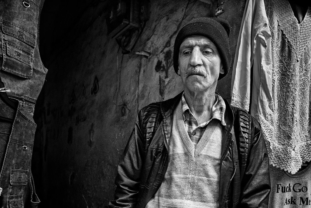An older person wearing a cap at the entrance to a passage.